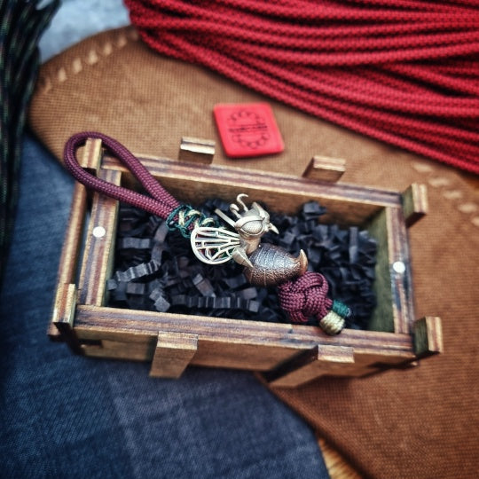 Decorative keychain with intricate design in a wooden box on a textured surface.