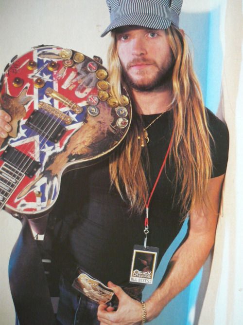Person holding a guitar with a colorful design, wearing a cap and black shirt.